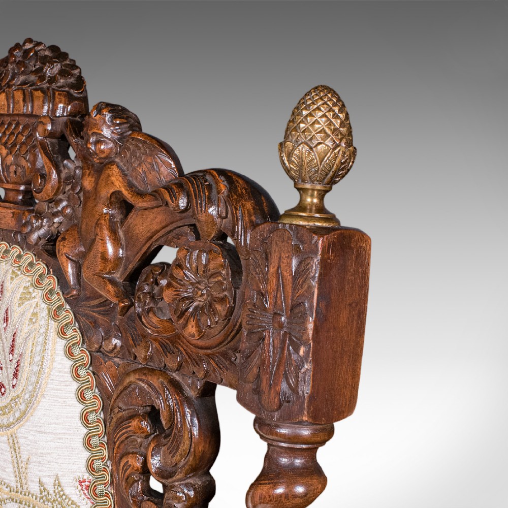 A pair of carved dark oak armchairs featuring barley twist uprights, intricate cherub carvings, and cream floral tapestry upholstery with red fringe trim. View IX