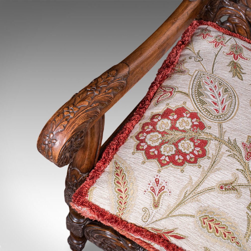 A pair of carved dark oak armchairs featuring barley twist uprights, intricate cherub carvings, and cream floral tapestry upholstery with red fringe trim. View X