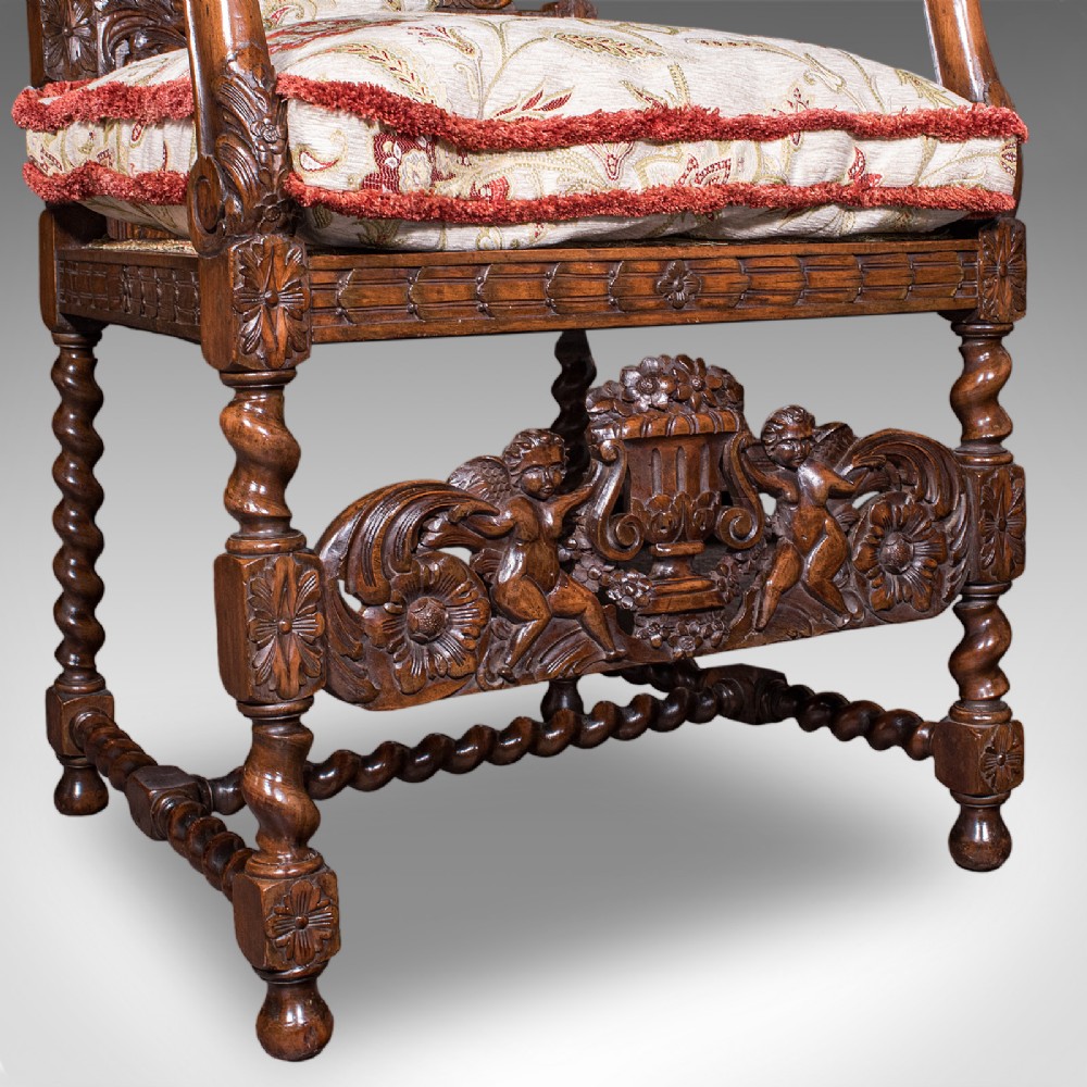 A pair of carved dark oak armchairs featuring barley twist uprights, intricate cherub carvings, and cream floral tapestry upholstery with red fringe trim. View XII