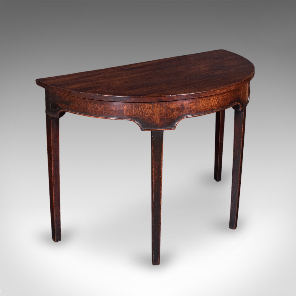 An antique dark mahogany demi-lune console table featuring tapered legs and a curved frieze.