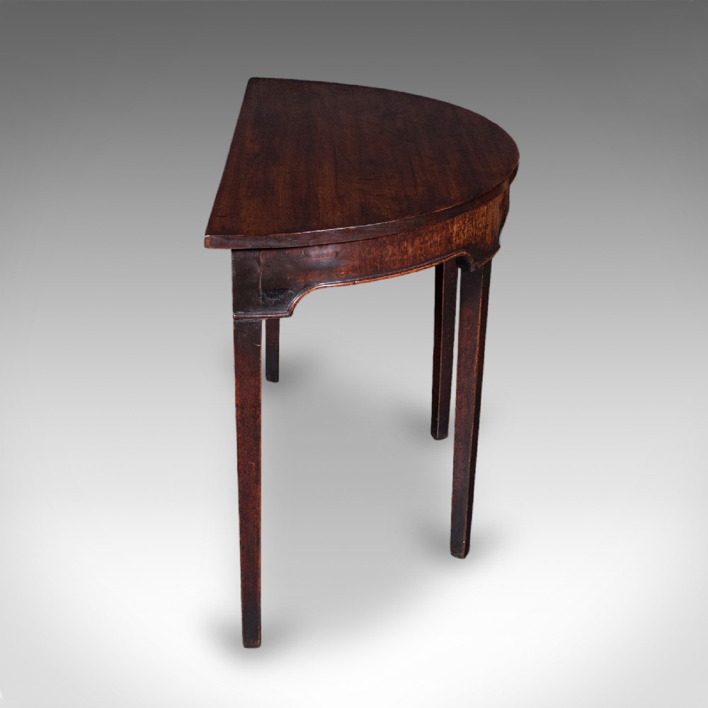 An antique dark mahogany demi-lune console table featuring tapered legs and a curved frieze. View III