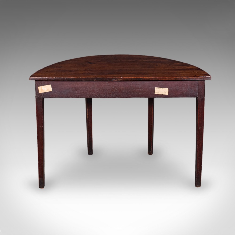 An antique dark mahogany demi-lune console table featuring tapered legs and a curved frieze. View IV