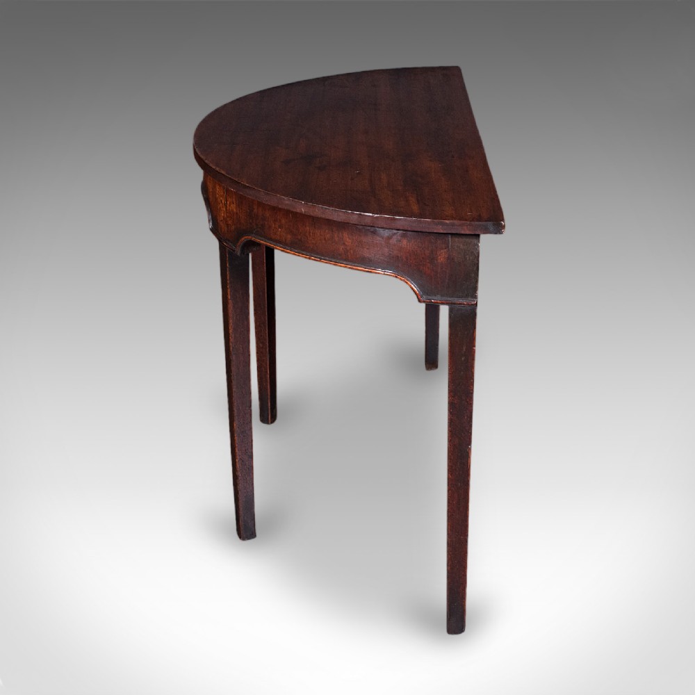An antique dark mahogany demi-lune console table featuring tapered legs and a curved frieze. View V