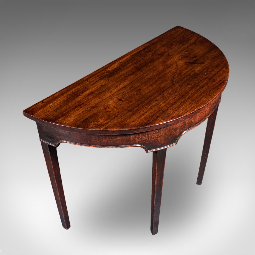 An antique dark mahogany demi-lune console table featuring tapered legs and a curved frieze. View VI