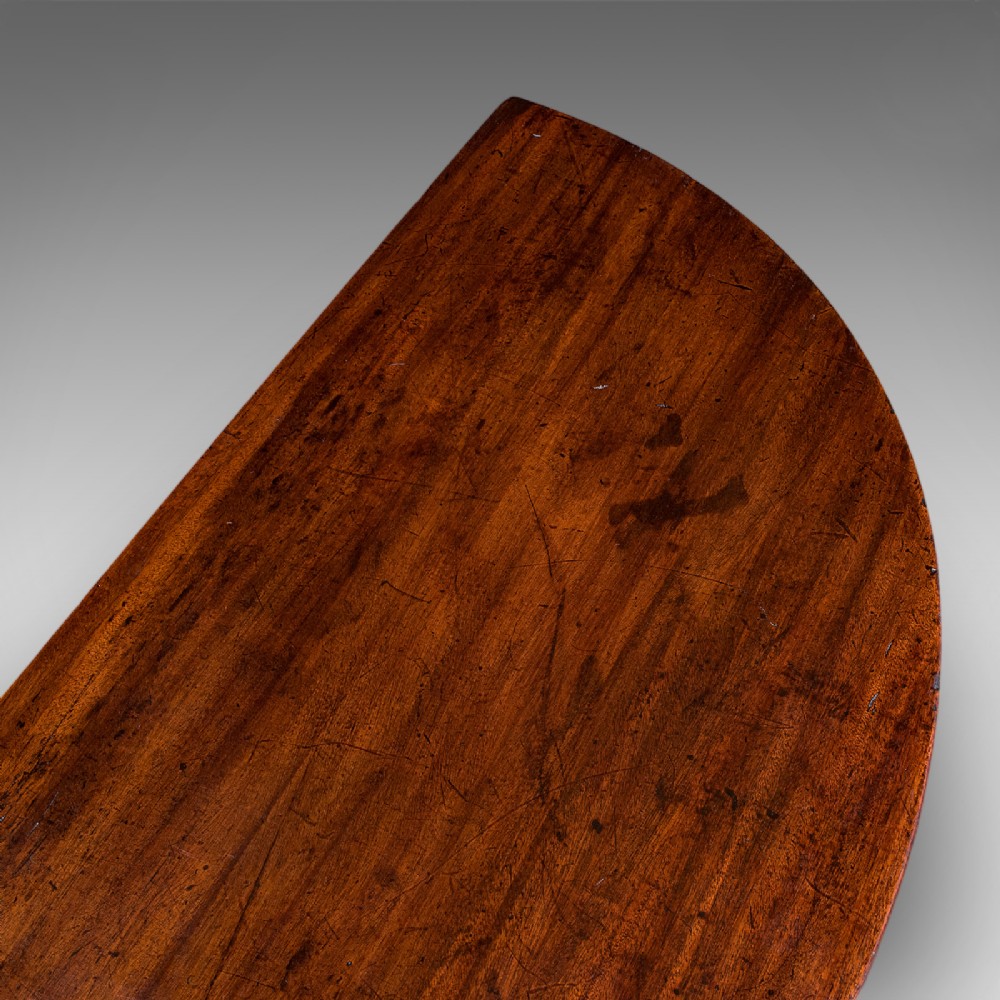 An antique dark mahogany demi-lune console table featuring tapered legs and a curved frieze. View VII