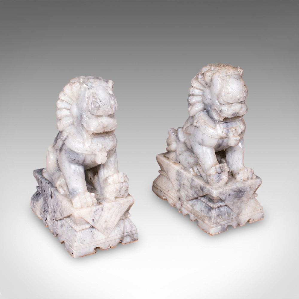 A pair of hand-carved mottled grey soapstone guardian lion bookends mounted on carved pedestals.