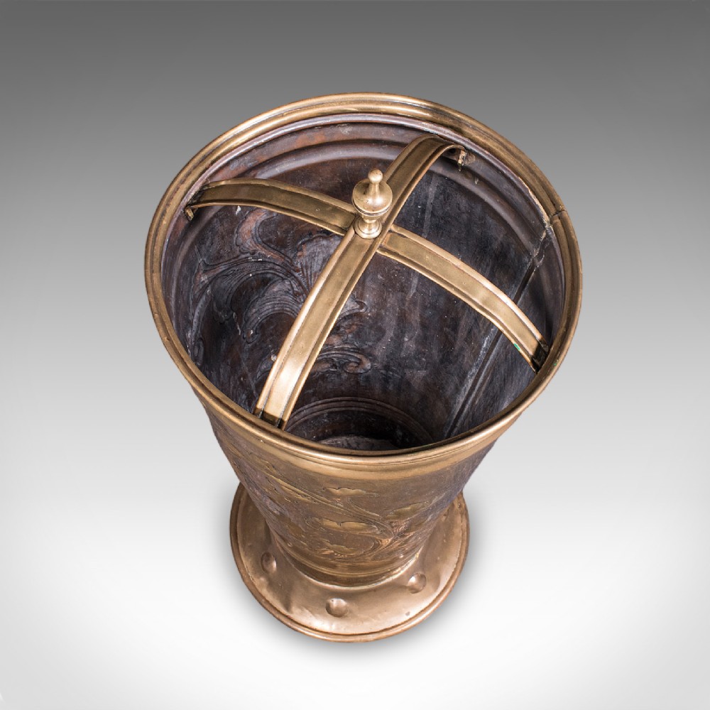 An antique tapered brass umbrella stand featuring embossed Dutch windmill motifs, top dividers with a turned brass finial, and a flared base. View VI