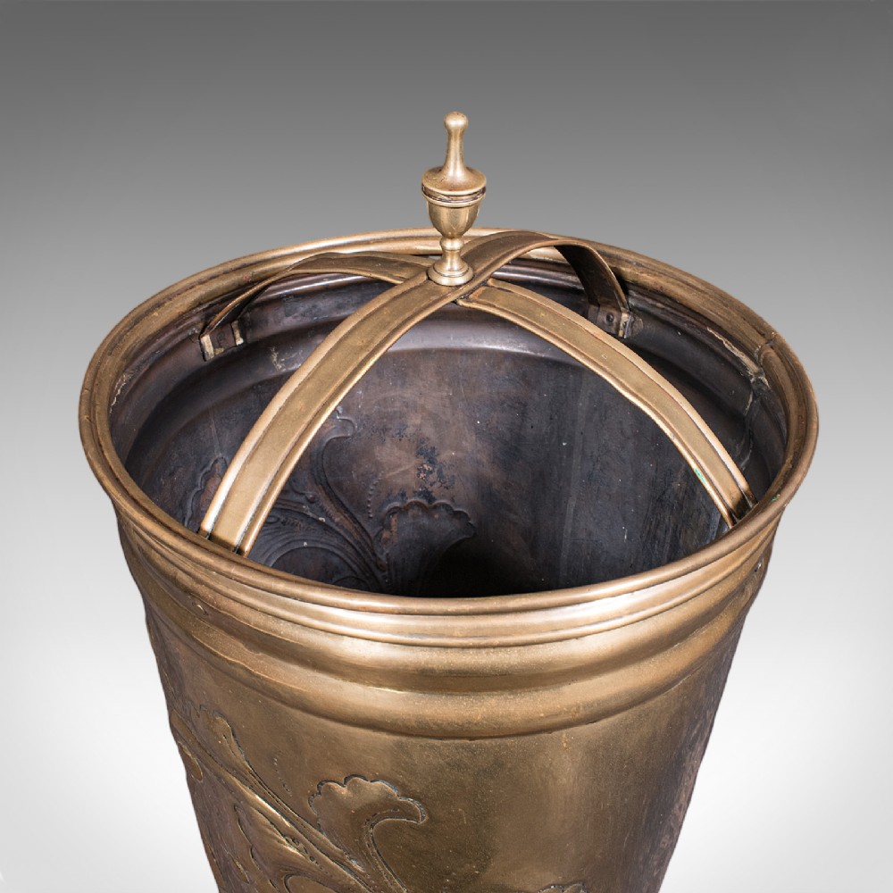 An antique tapered brass umbrella stand featuring embossed Dutch windmill motifs, top dividers with a turned brass finial, and a flared base. View VII