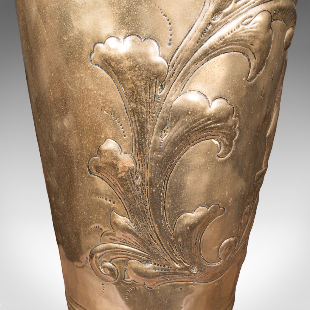 An antique tapered brass umbrella stand featuring embossed Dutch windmill motifs, top dividers with a turned brass finial, and a flared base. View X
