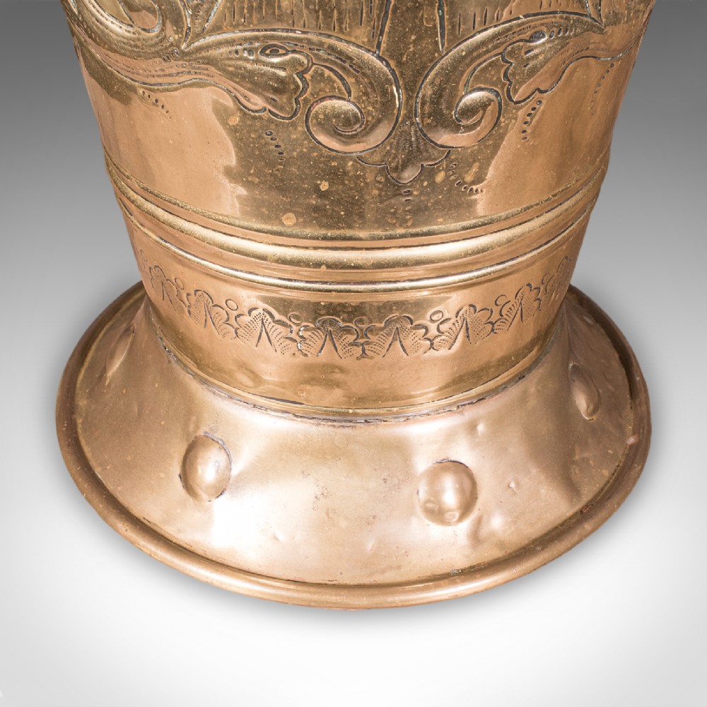 An antique tapered brass umbrella stand featuring embossed Dutch windmill motifs, top dividers with a turned brass finial, and a flared base. View XI