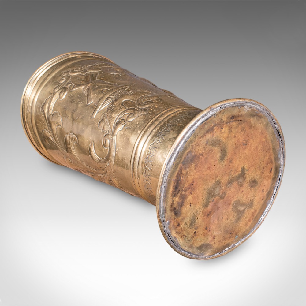An antique tapered brass umbrella stand featuring embossed Dutch windmill motifs, top dividers with a turned brass finial, and a flared base. View XII