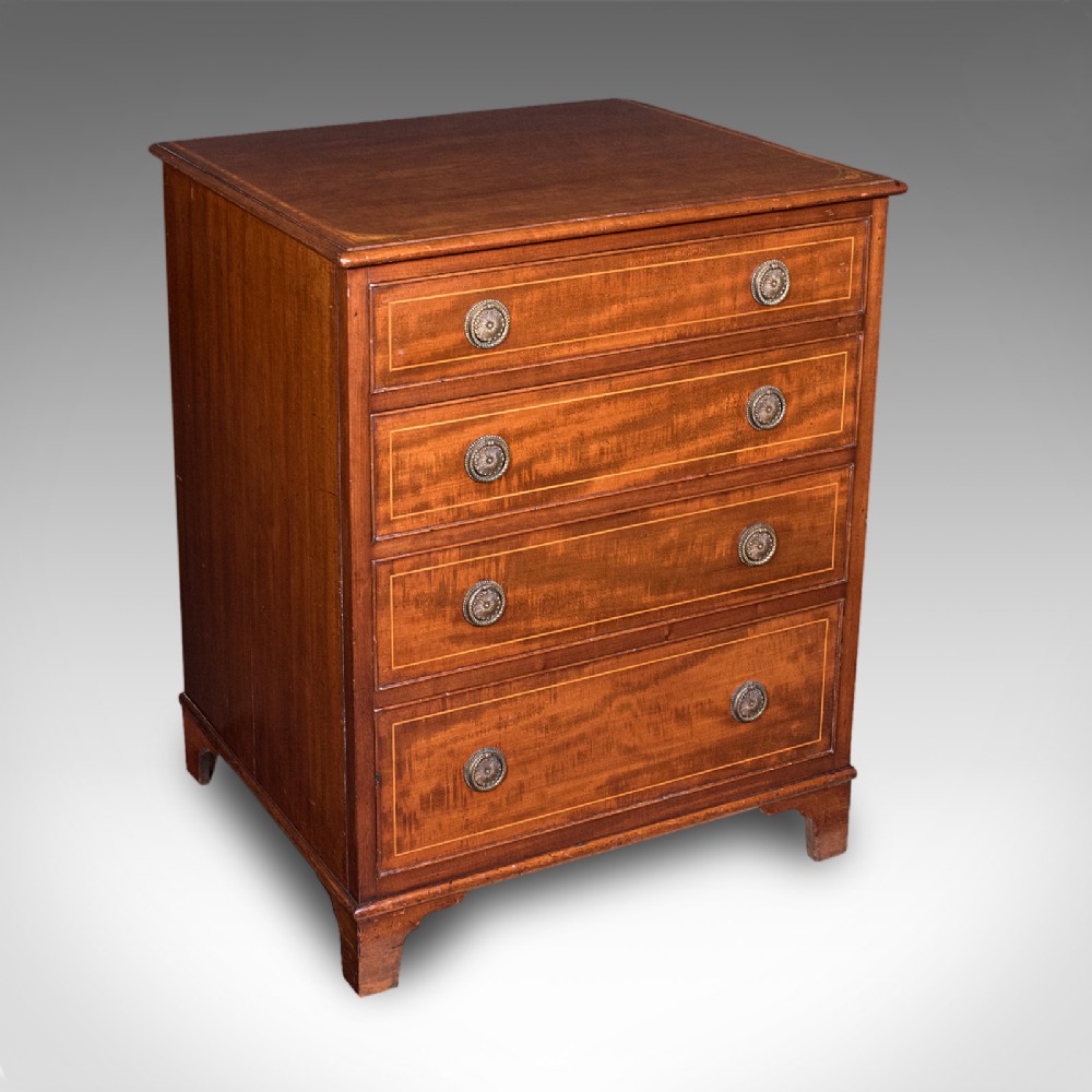 An antique mahogany small chest of drawers featuring four graduated inlaid drawers, circular brass ring pull handles, and bracket feet.