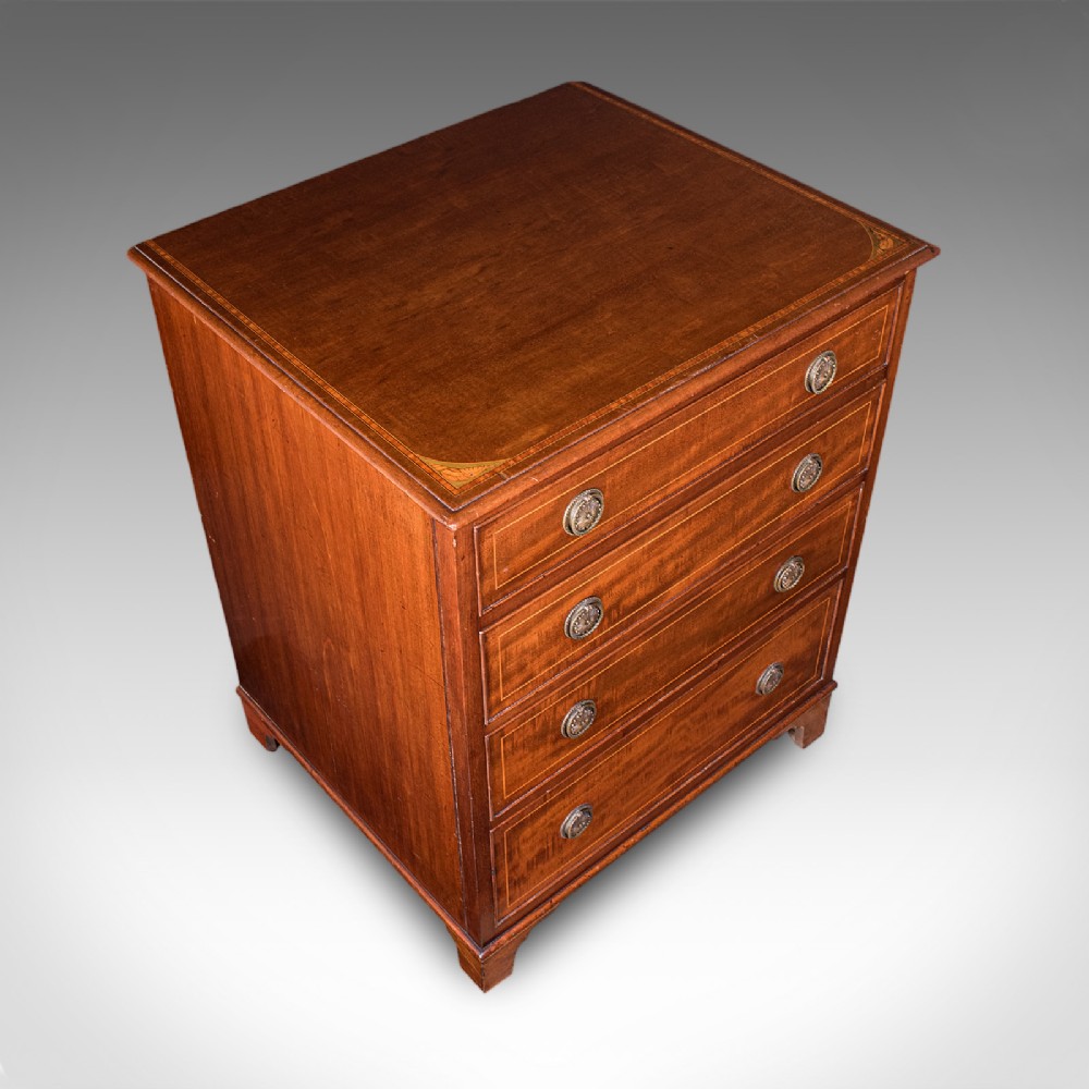 An antique mahogany small chest of drawers featuring four graduated inlaid drawers, circular brass ring pull handles, and bracket feet. View VII