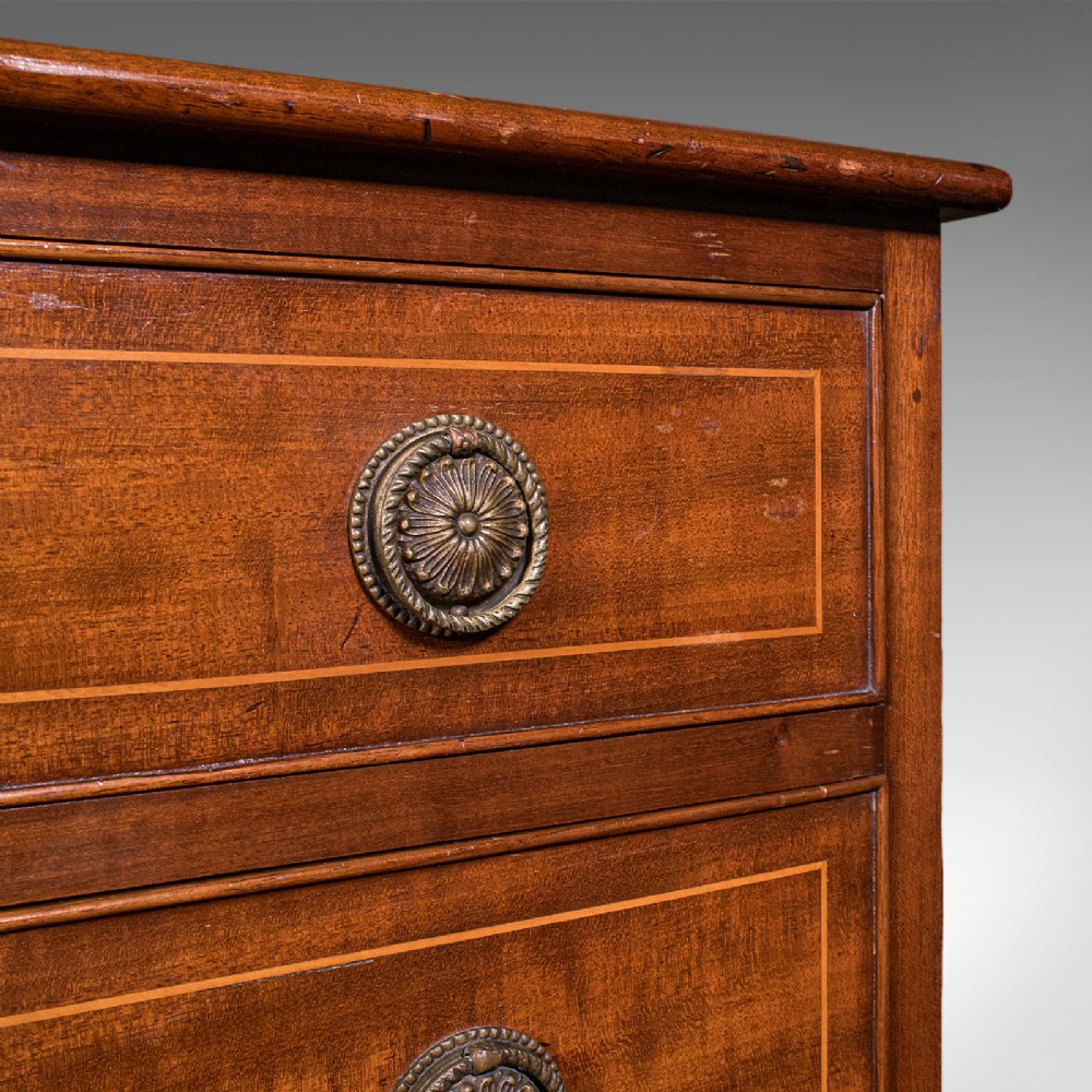 An antique mahogany small chest of drawers featuring four graduated inlaid drawers, circular brass ring pull handles, and bracket feet. View X