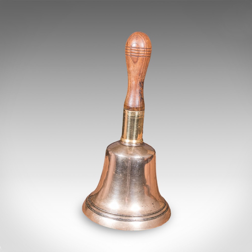 Victorian hand bell featuring a polished brass bell body with a turned beech handle set on a circular wooden stand. View IV