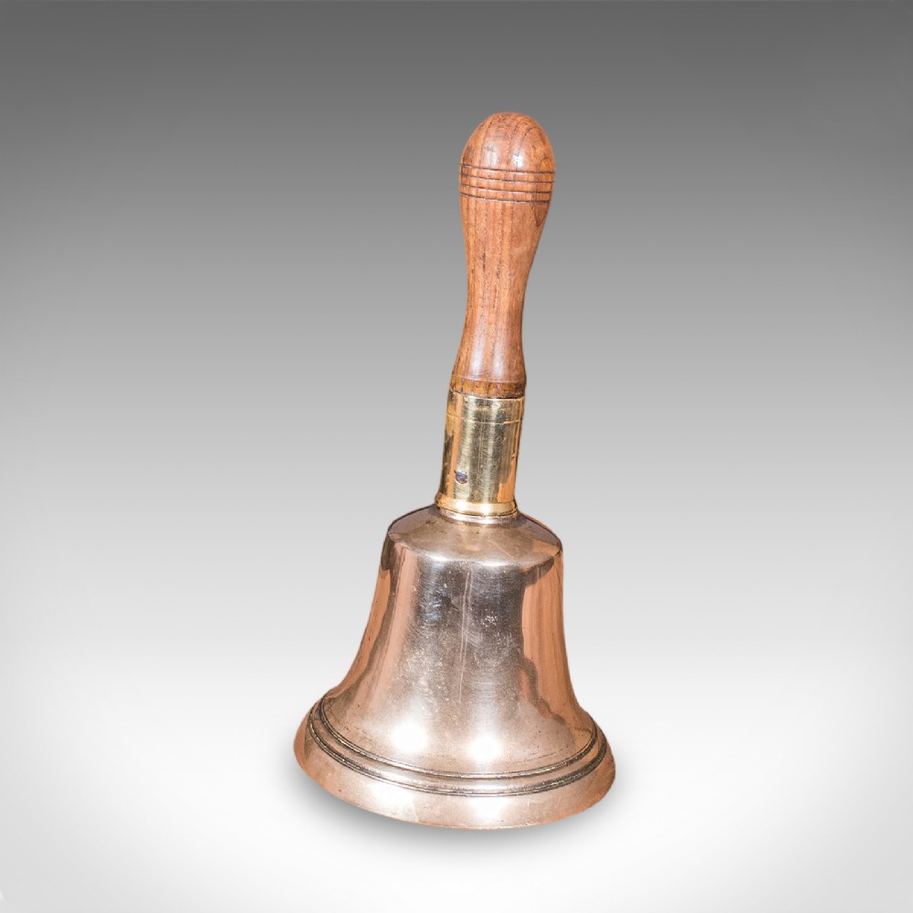 Victorian hand bell featuring a polished brass bell body with a turned beech handle set on a circular wooden stand. View V