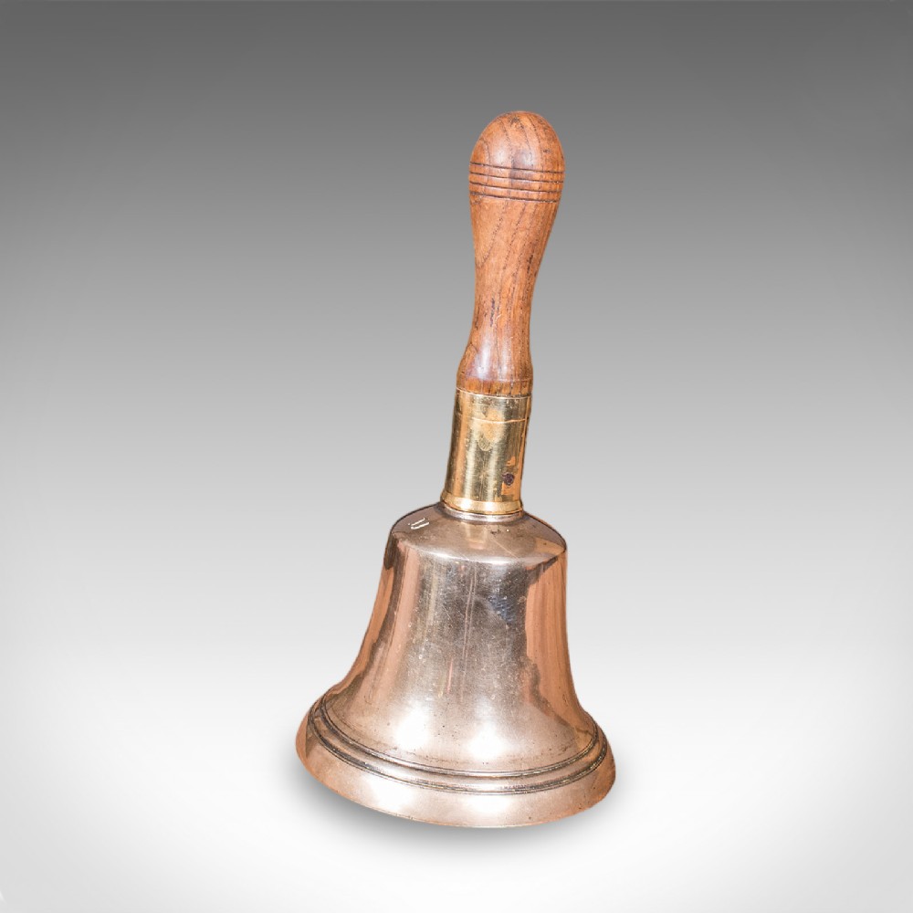Victorian hand bell featuring a polished brass bell body with a turned beech handle set on a circular wooden stand. View VI