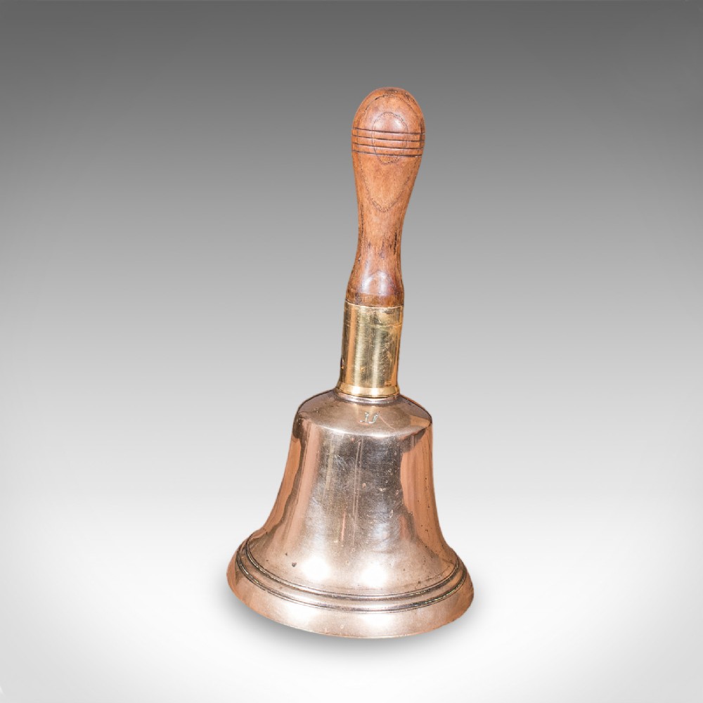 Victorian hand bell featuring a polished brass bell body with a turned beech handle set on a circular wooden stand. View VII