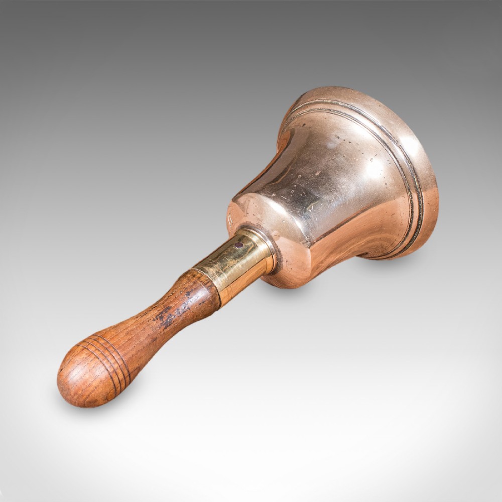 Victorian hand bell featuring a polished brass bell body with a turned beech handle set on a circular wooden stand. View X