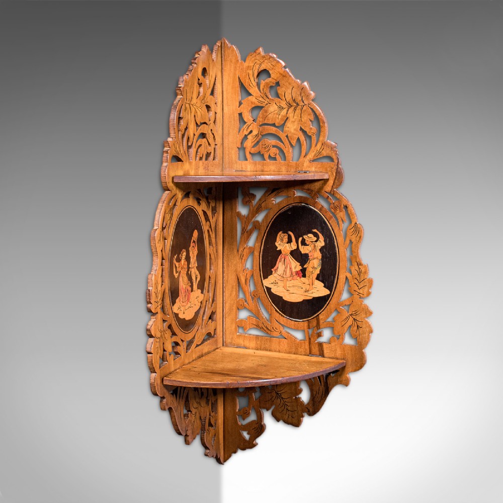A Victorian Italian walnut corner display shelf featuring two tiers, openwork foliage fretwork borders, and oval marquetry panels depicting folk dancers.
