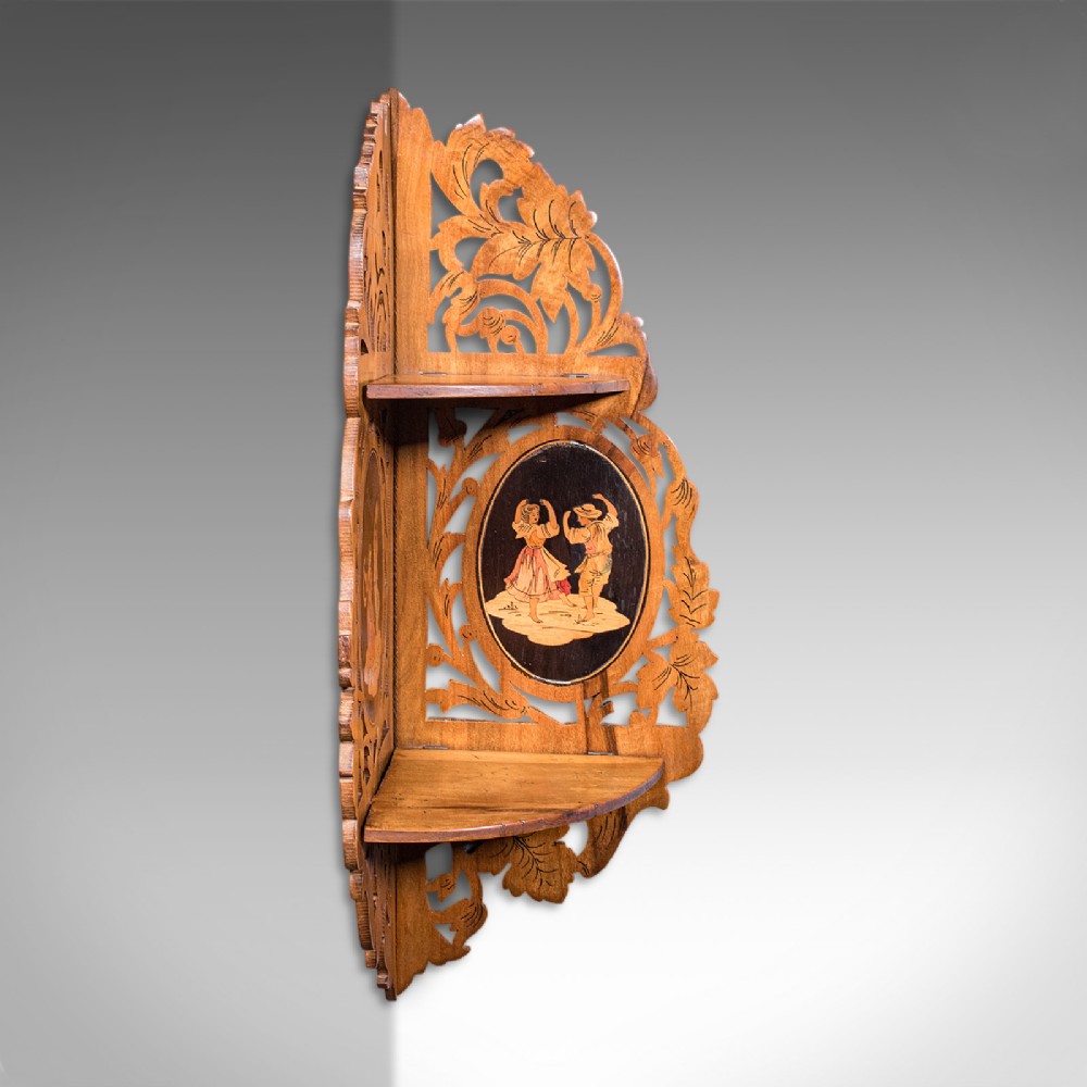 A Victorian Italian walnut corner display shelf featuring two tiers, openwork foliage fretwork borders, and oval marquetry panels depicting folk dancers. View III