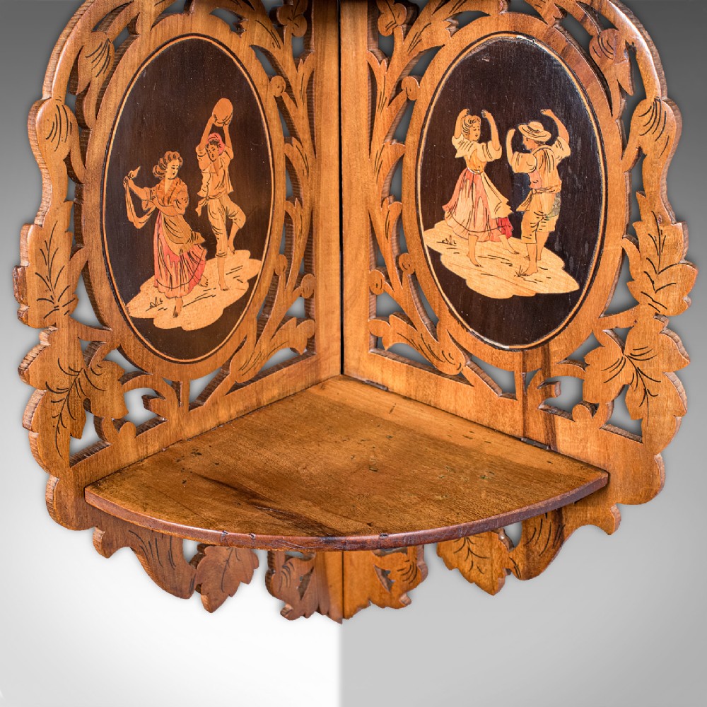 A Victorian Italian walnut corner display shelf featuring two tiers, openwork foliage fretwork borders, and oval marquetry panels depicting folk dancers. View VI