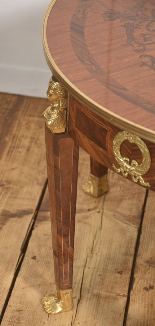 A round Louis XVI style coffee table featuring wood marquetry, warm brown veneers, tapered square legs, and decorative gilt brass female bust mounts. View V