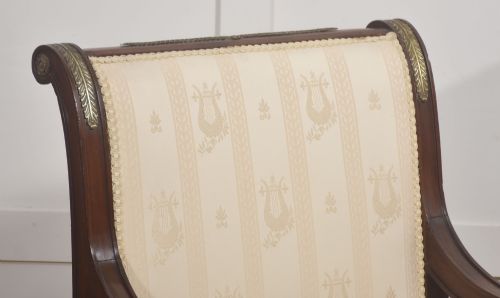 fig 2. An Empire style mahogany armchair featuring cream upholstered silk fabric with lyre motifs, winged sphinx arm supports, and gilt brass winged lion front legs.