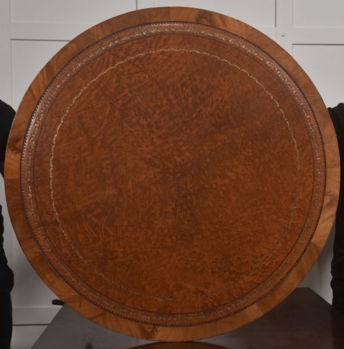 fig 1. A circular Regency style mahogany coffee table featuring an inset brown leather top with gold leaf tooling, supported by a central pedestal and four splayed legs fitted with brass castors.