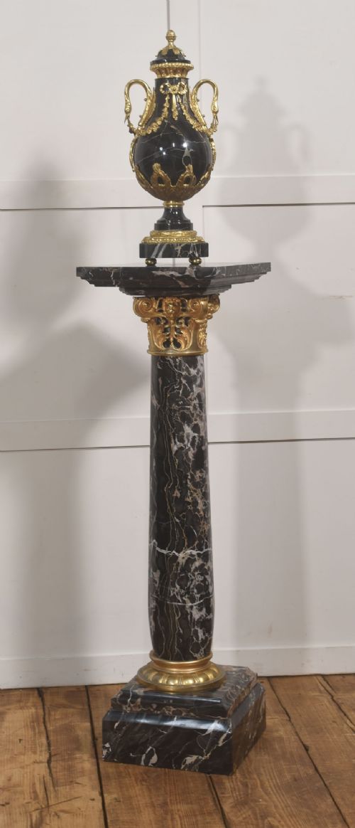 A black veined-marble urn with two handles and gilt-metal mounts resting on a matching cylindrical black marble pedestal with a Corinthian capital. View IX