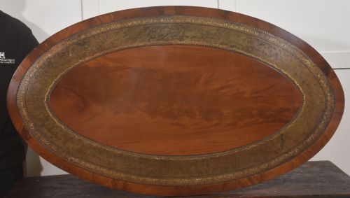fig 1. An oval mahogany coffee table featuring an inset green tooled leather border, a central turned pedestal stem, four swept legs, and brass castors.