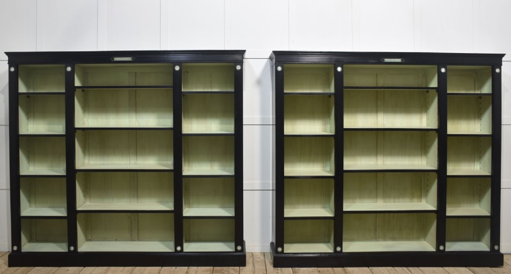 A pair of large ebonised open bookcases featuring three vertical shelving sections with pale green painted interiors and circular ceramic plaque detailing.