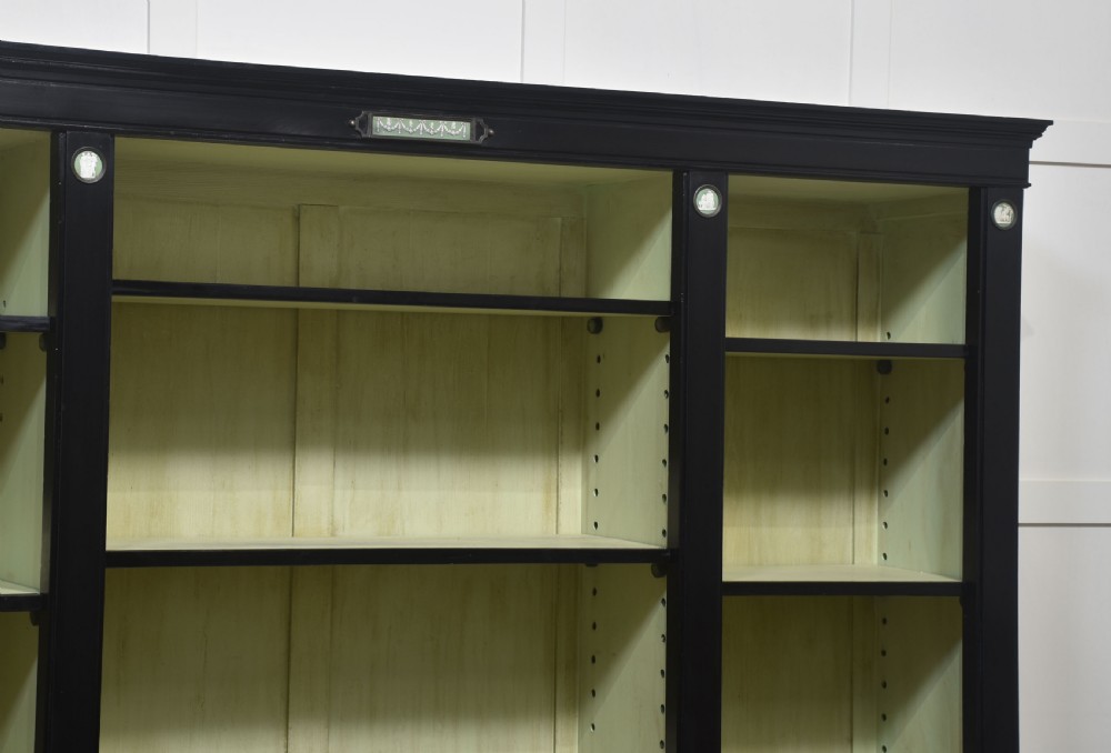 A pair of large ebonised open bookcases featuring three vertical shelving sections with pale green painted interiors and circular ceramic plaque detailing. View V
