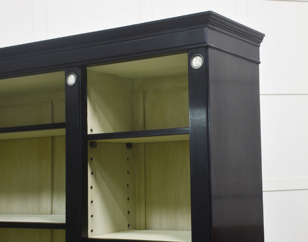 A pair of large ebonised open bookcases featuring three vertical shelving sections with pale green painted interiors and circular ceramic plaque detailing. View VI