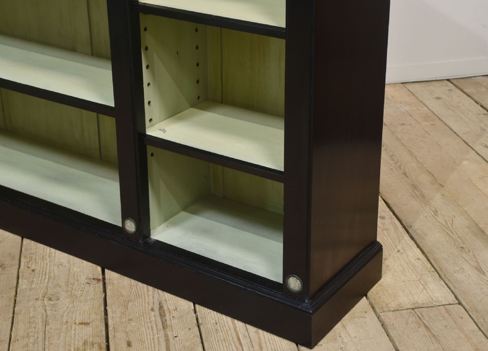 A pair of large ebonised open bookcases featuring three vertical shelving sections with pale green painted interiors and circular ceramic plaque detailing. View VII