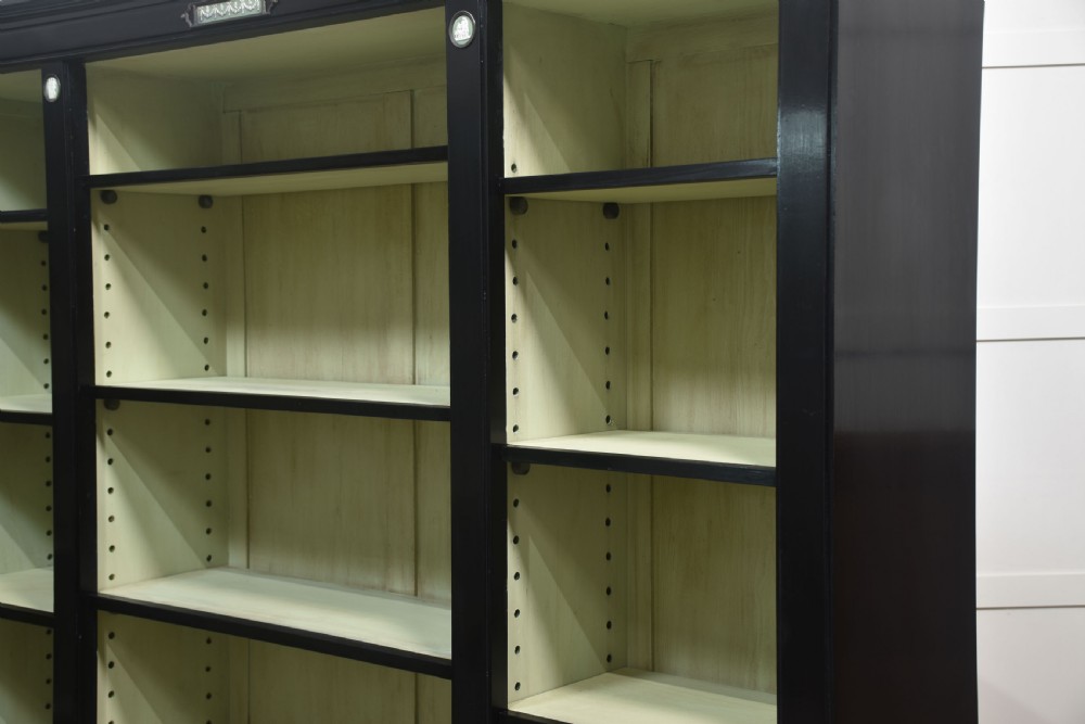 A pair of large ebonised open bookcases featuring three vertical shelving sections with pale green painted interiors and circular ceramic plaque detailing. View IX