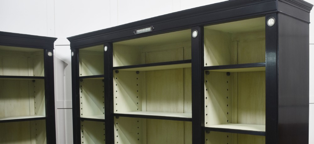 A pair of large ebonised open bookcases featuring three vertical shelving sections with pale green painted interiors and circular ceramic plaque detailing. View X
