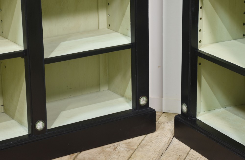 A pair of large ebonised open bookcases featuring three vertical shelving sections with pale green painted interiors and circular ceramic plaque detailing. View XI