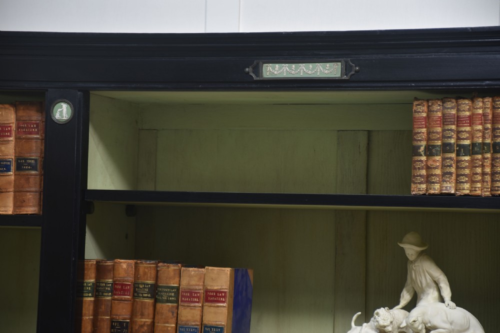 A pair of large ebonised open bookcases featuring three vertical shelving sections with pale green painted interiors and circular ceramic plaque detailing. View XIII