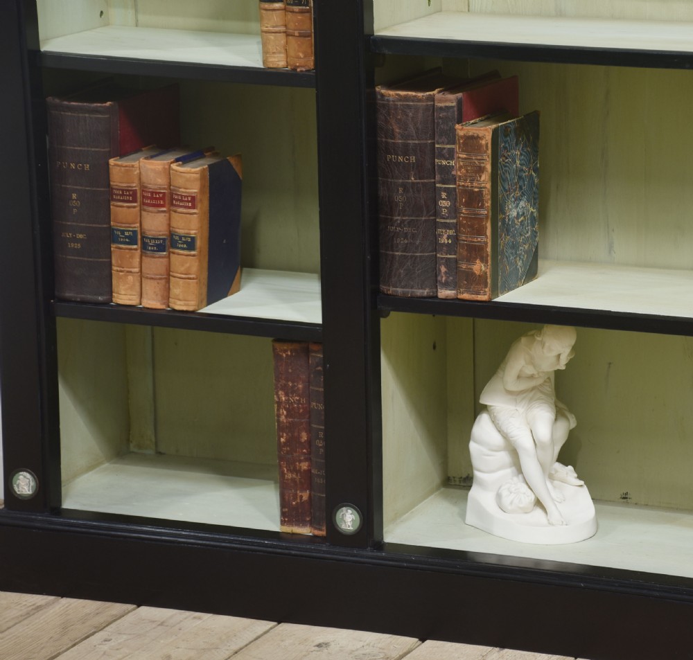 A pair of large ebonised open bookcases featuring three vertical shelving sections with pale green painted interiors and circular ceramic plaque detailing. View XIV