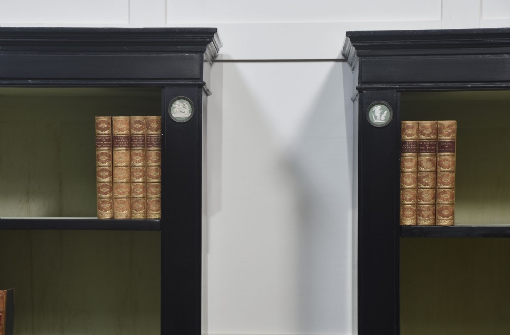 A pair of large ebonised open bookcases featuring three vertical shelving sections with pale green painted interiors and circular ceramic plaque detailing. View XV