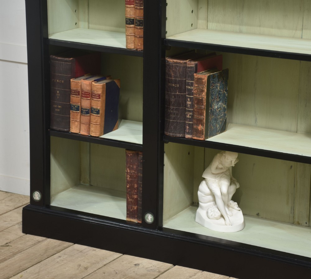 A pair of large ebonised open bookcases featuring three vertical shelving sections with pale green painted interiors and circular ceramic plaque detailing. View XVI