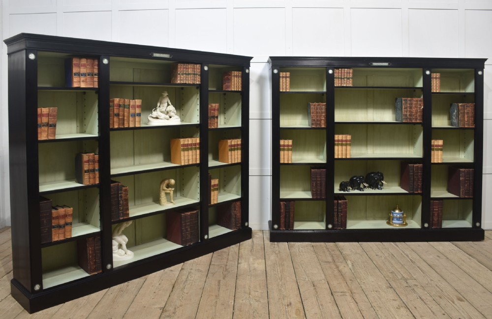 A pair of large ebonised open bookcases featuring three vertical shelving sections with pale green painted interiors and circular ceramic plaque detailing. View XVII