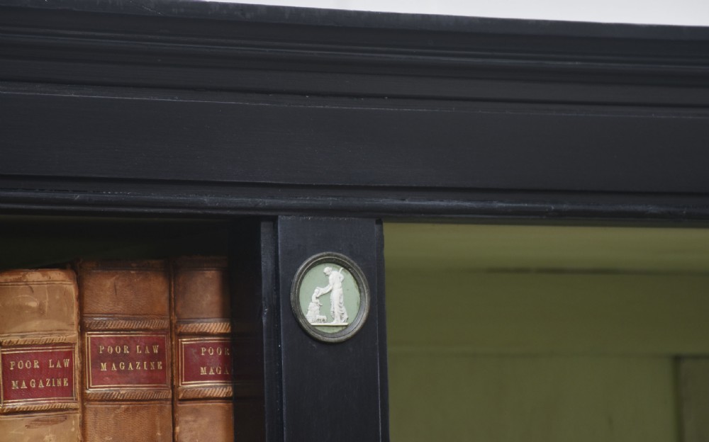 A pair of large ebonised open bookcases featuring three vertical shelving sections with pale green painted interiors and circular ceramic plaque detailing. View XXI