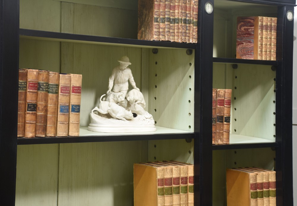 A pair of large ebonised open bookcases featuring three vertical shelving sections with pale green painted interiors and circular ceramic plaque detailing. View XXII