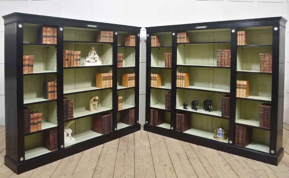 A pair of large ebonised open bookcases featuring three vertical shelving sections with pale green painted interiors and circular ceramic plaque detailing. View XXIII