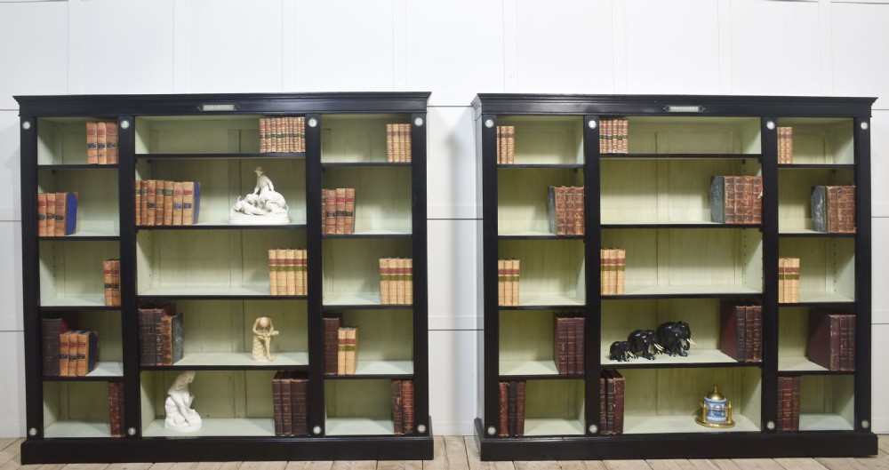 A pair of large ebonised open bookcases featuring three vertical shelving sections with pale green painted interiors and circular ceramic plaque detailing. View XXIV