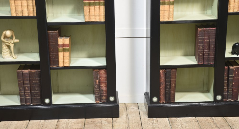 A pair of large ebonised open bookcases featuring three vertical shelving sections with pale green painted interiors and circular ceramic plaque detailing. View XXV