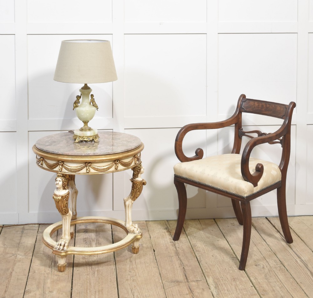 A circular Neoclassical occasional table with a polished pink marble top, cream-painted frame, gold leaf drapery swags, and carved term legs ending in paw feet. View II