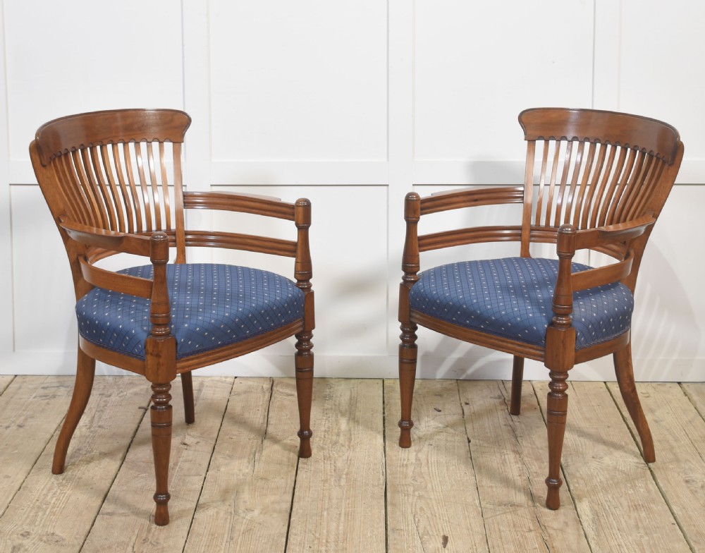 A pair of mahogany elbow chairs featuring slatted curved backs, turned front legs, and blue patterned upholstered seats.